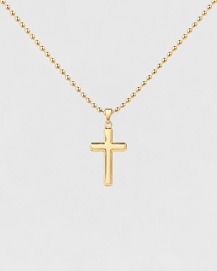 Cross necklace in gold-tone stainless steel on a light grey background