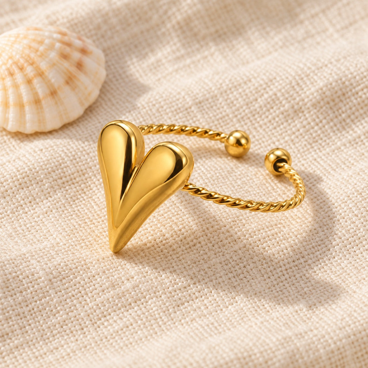 MARÉA Heart Twist Ring gold open ring with a polished heart and twisted band on linen