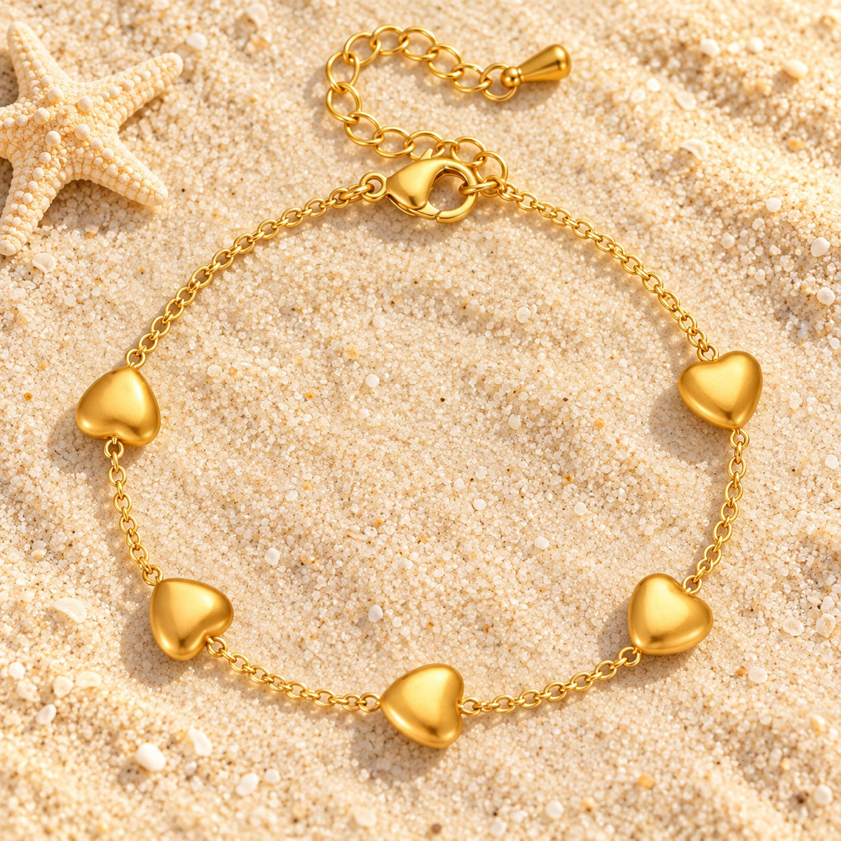 MARÉA Sweetheart Bracelet fine gold chain with five puffed hearts on sand with a starfish