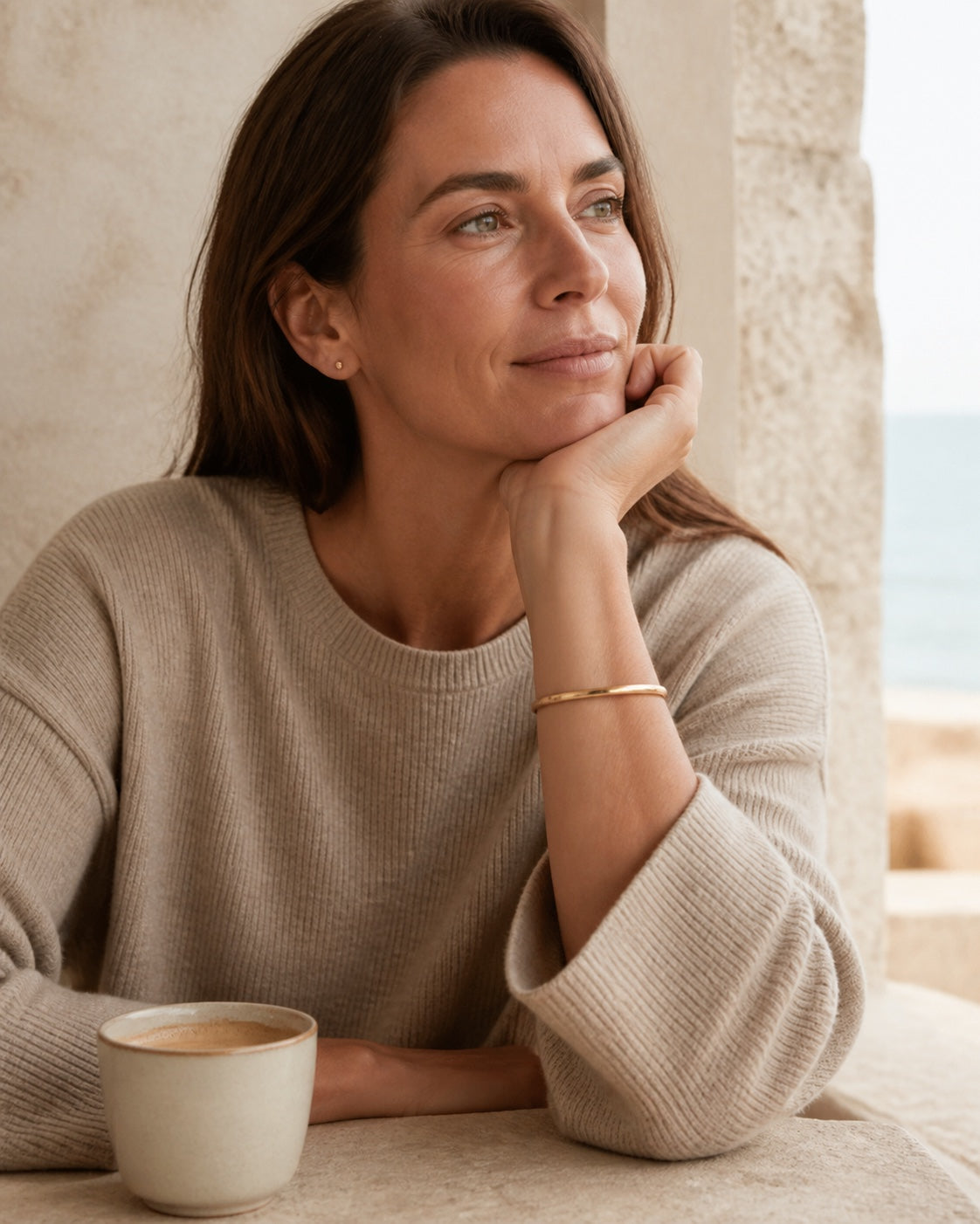 Woman resting her chin on her hand, gold MAREA Shoreline Bangle on her wrist
