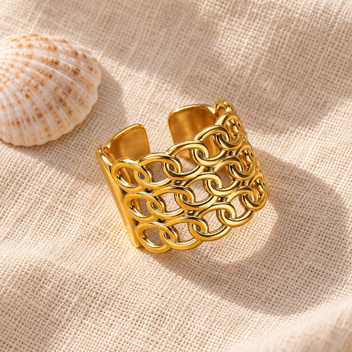 MARÉA Chain Link Ring wide gold open ring of interlocking chain links on linen with a shell