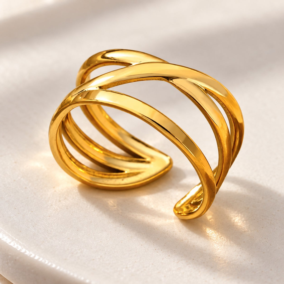 MARÉA Crossover Ring gold open ring with crossing bands on white ceramic