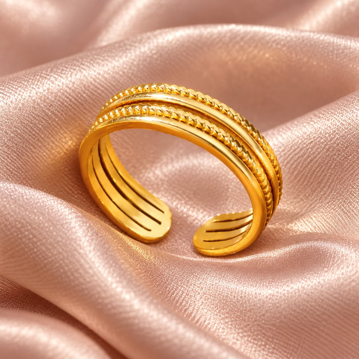 MARÉA Ridge Ring gold open ring with four parallel bands, two with beaded texture, on pink silk