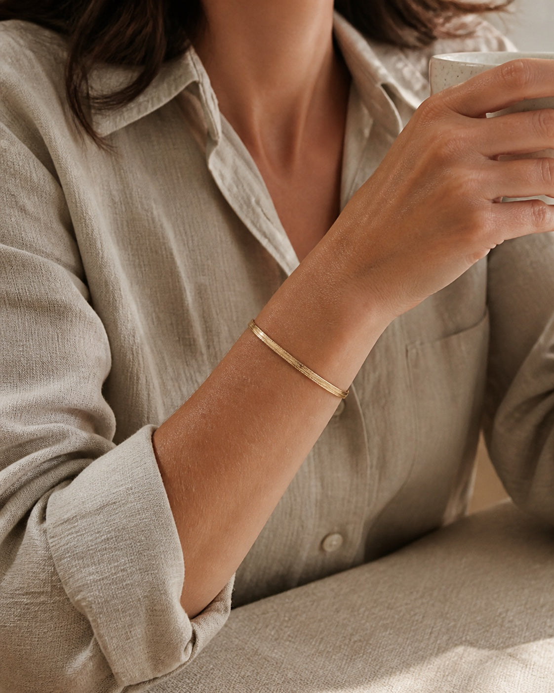 Woman with a coffee, gold MAREA Herringbone Bracelet on her wrist