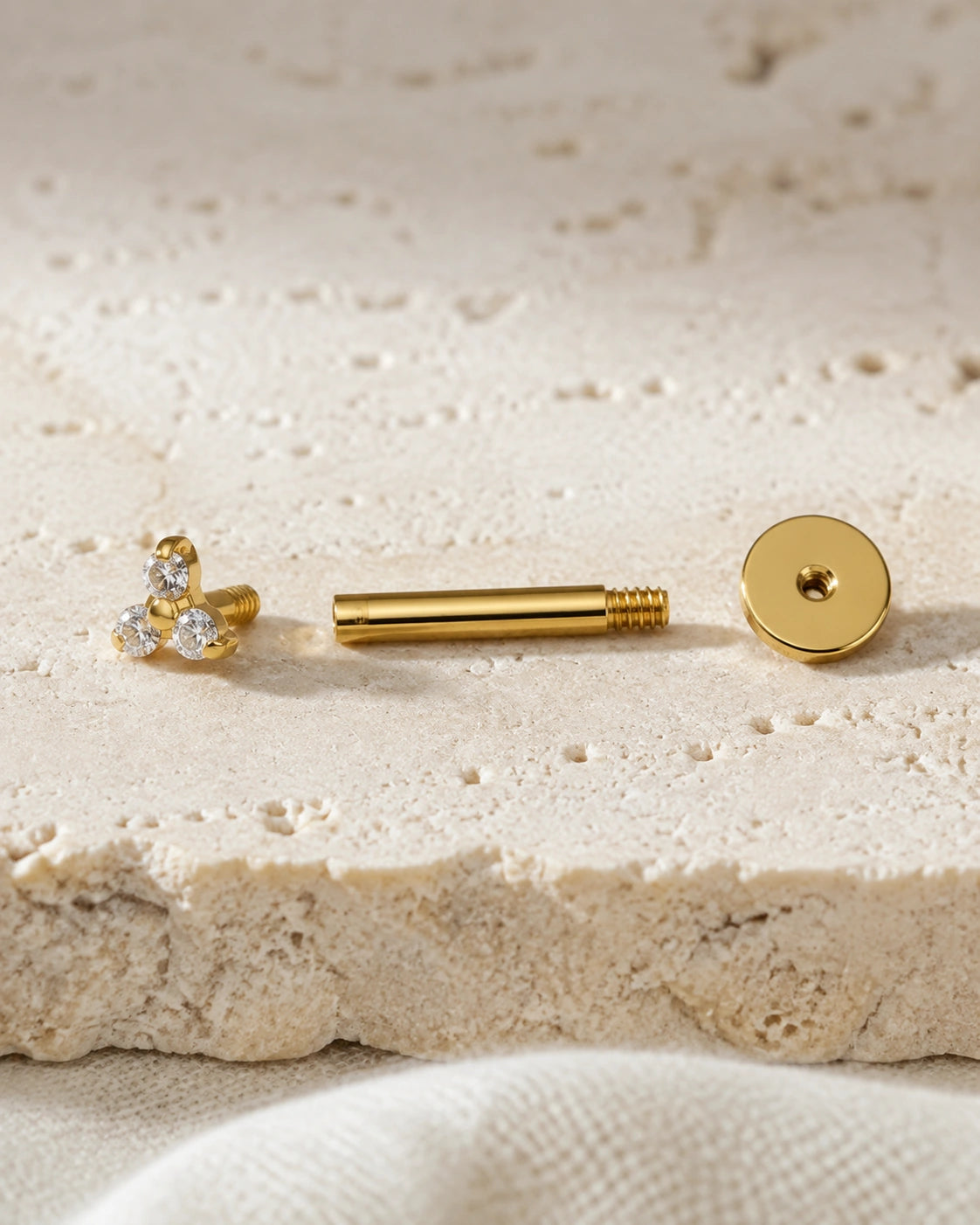 Macro of a gold MAREA titanium flatback stud disassembled — trinity top, threaded post, flat disc back