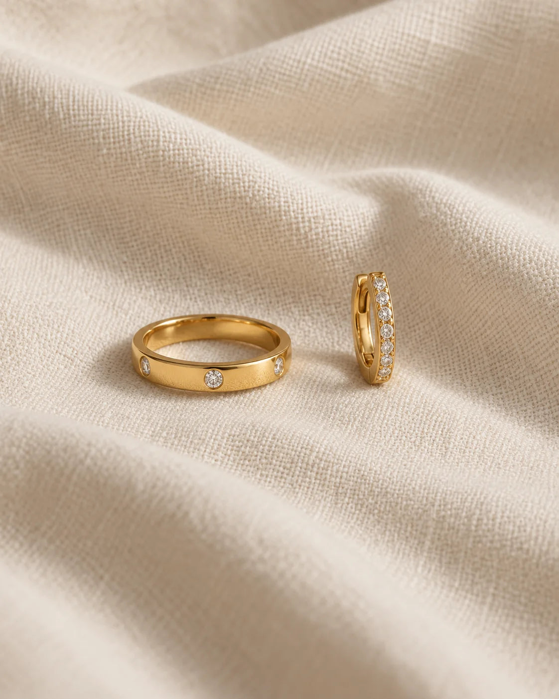The gold MARÉA pavé ring and pavé huggie set laid on cream linen