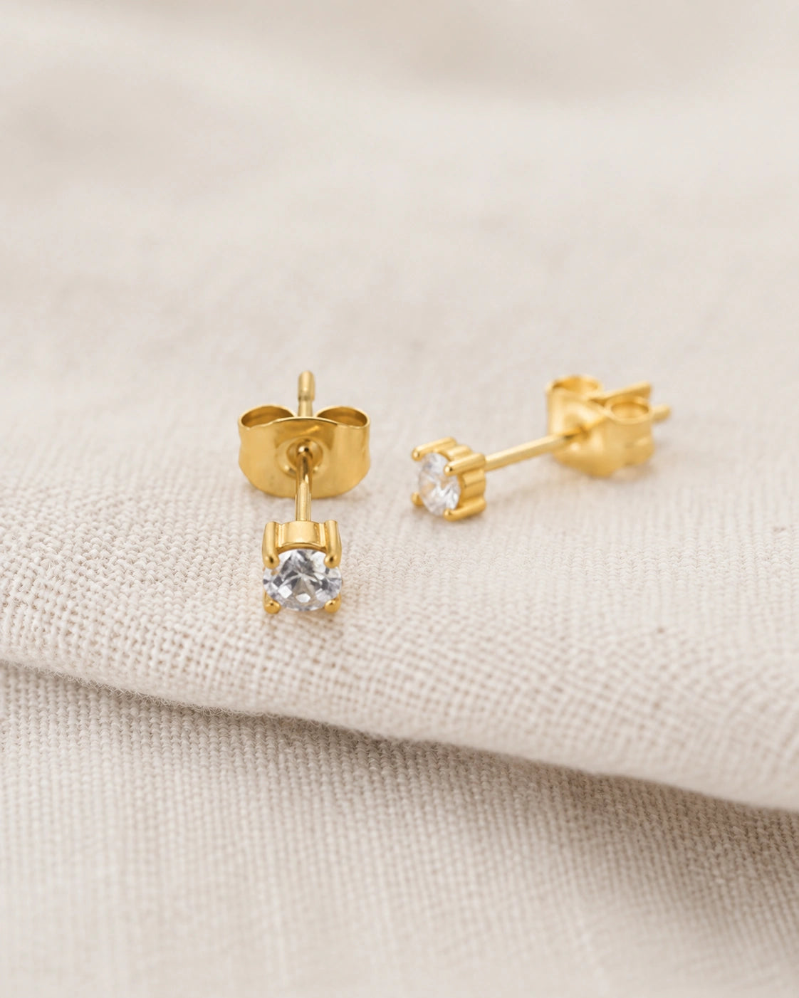 Gold cubic zirconia solitaire stud earrings by MAREA on natural linen
